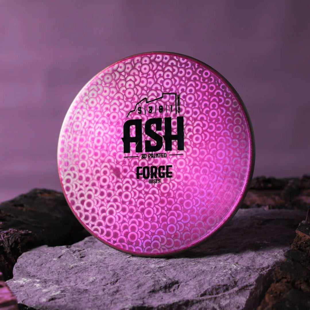 Pink and black disc golf disc with 'ASH' branding on a rock against a purple background